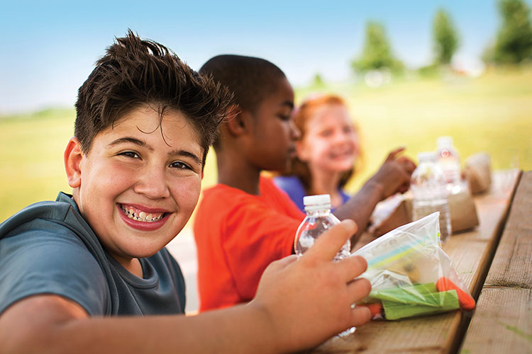 Boy smiles while eating lunch at picnic table
