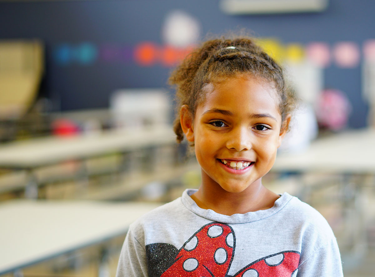 Young girl stands in classroom smiling