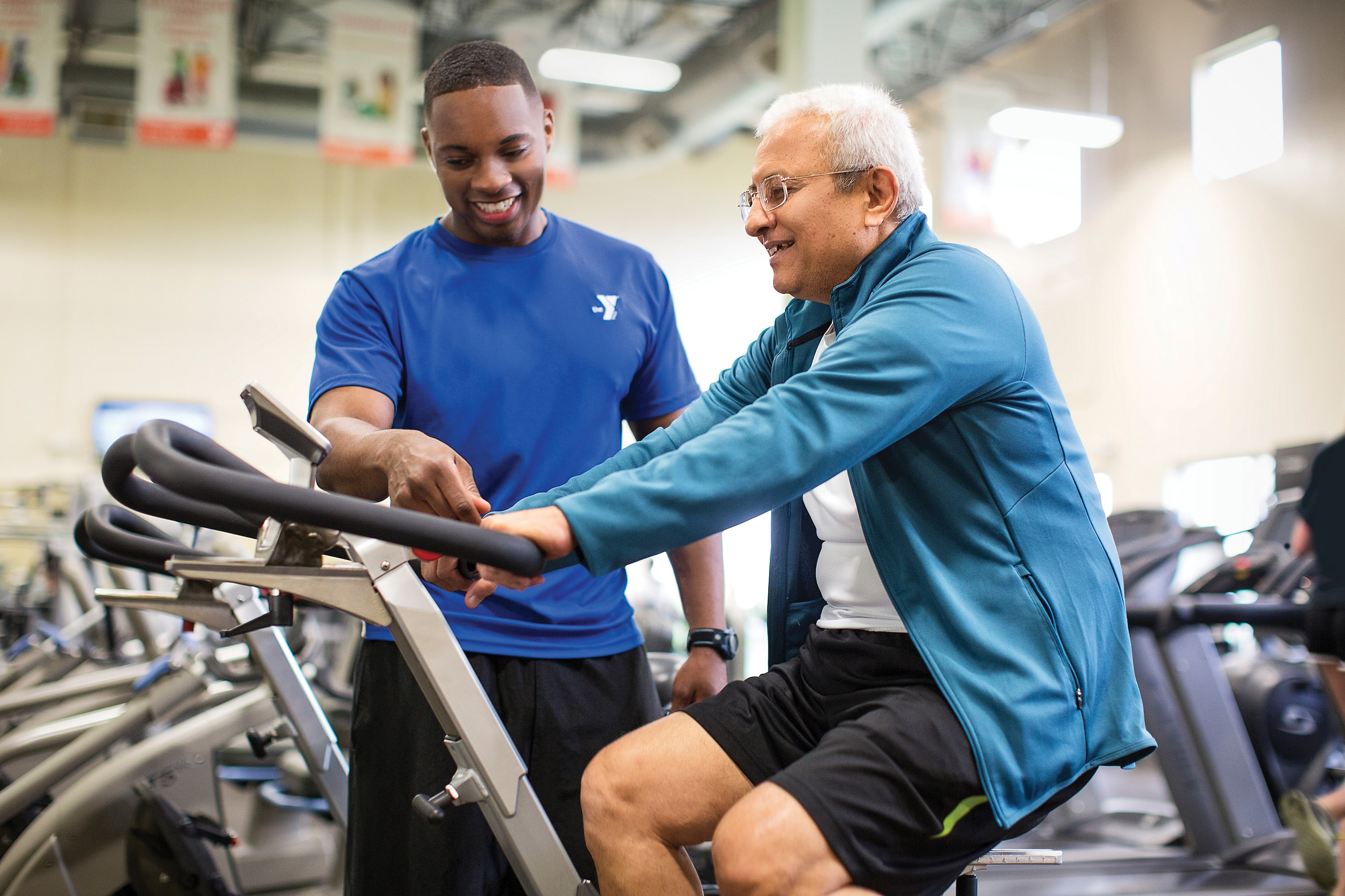 Personal trainer assists man on stationary bike