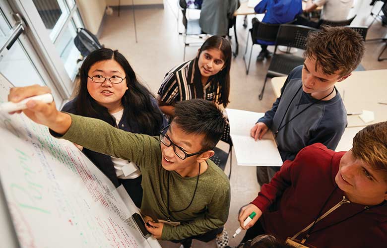 Group of teens working on project around a whiteboard